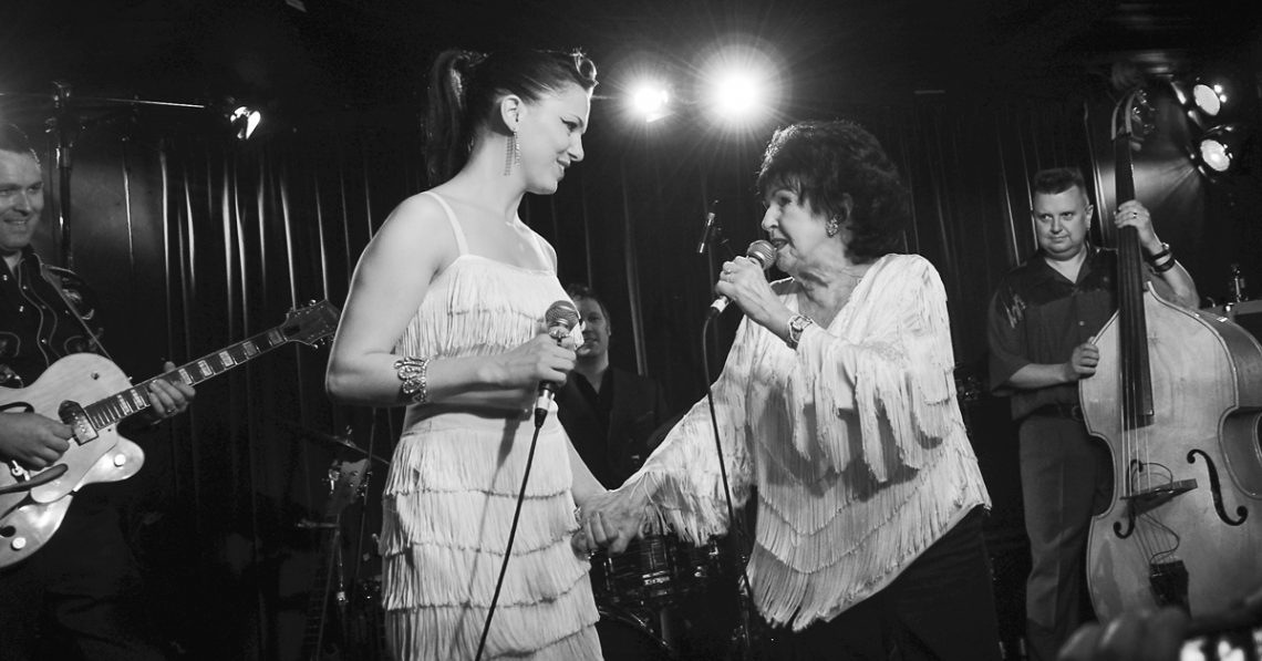 Imelda May and Wanda Jackson holding hands on stage at a gig